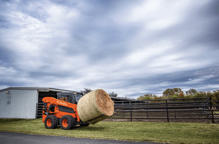 Skid steer moving a large hay bale