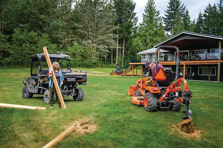 man on kubota tractor digging post hole with woman holding post by rtv