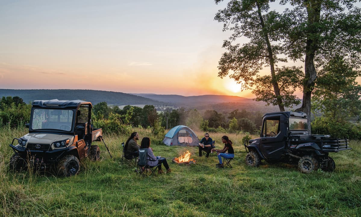 four people around fire with two Kubota RTVs