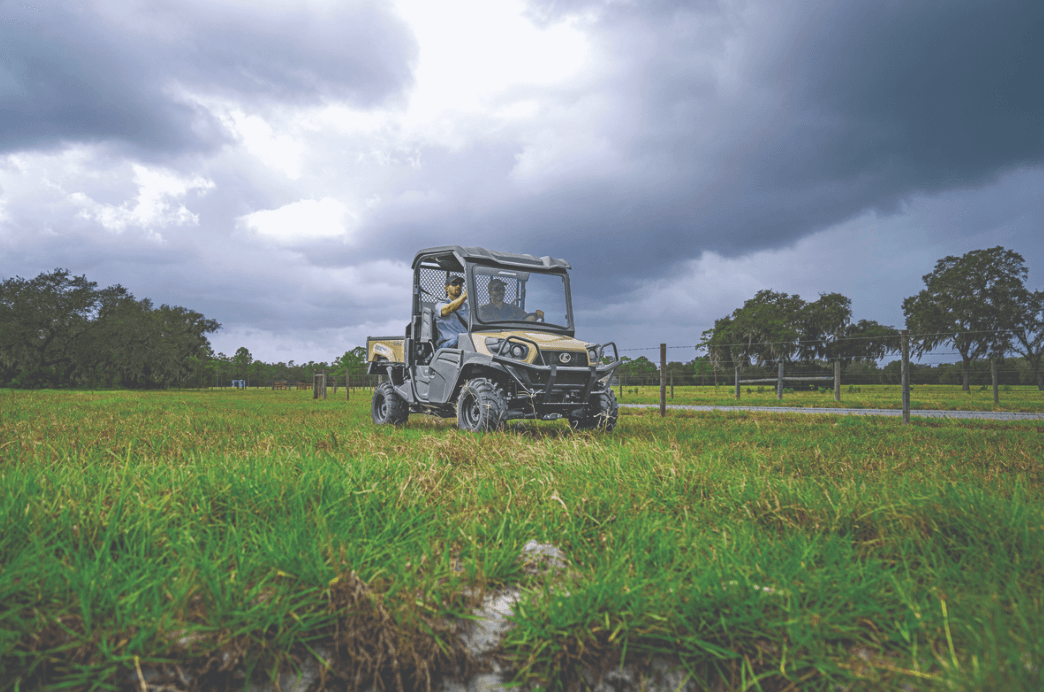 Men driving kubota sidekick through muddy field